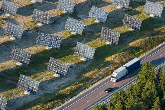 Luchtfoto van zonnepanelen langs een weg waar een vrachtwagen en een auto rijden.