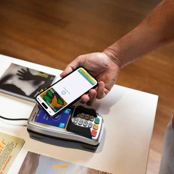 Een persoon doet een Apple Pay-betaling door een mobiele telefoon tegen een betaalautomaat te houden.