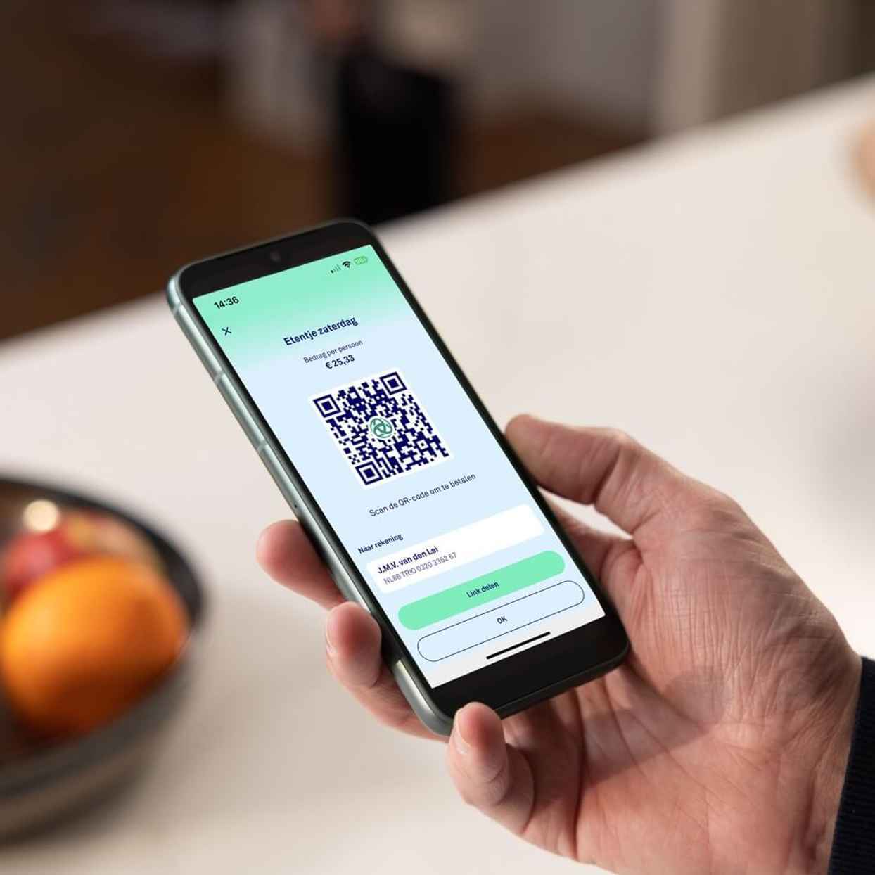 Persoon houdt met één hand een mobiele telefoon vast met daarop een betaalverzoek.