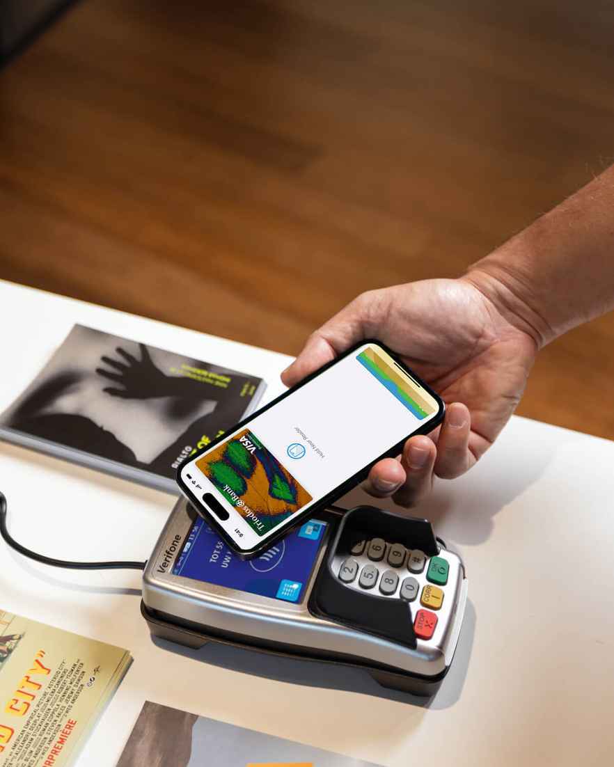 Een persoon doet een Apple Pay-betaling door een mobiele telefoon tegen een betaalautomaat te houden.