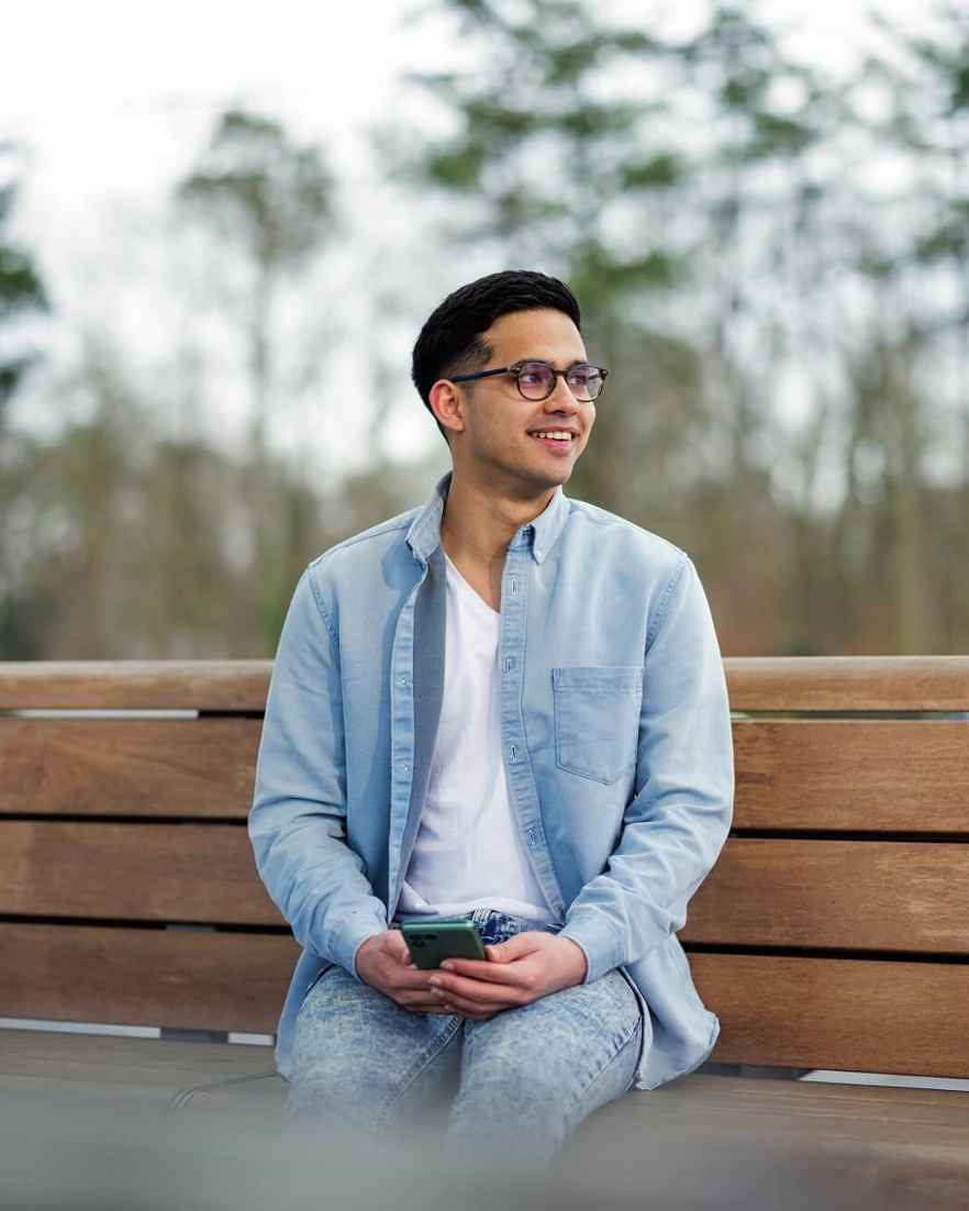 Man zit op een houten bank en houdt een telefoon in de hand.