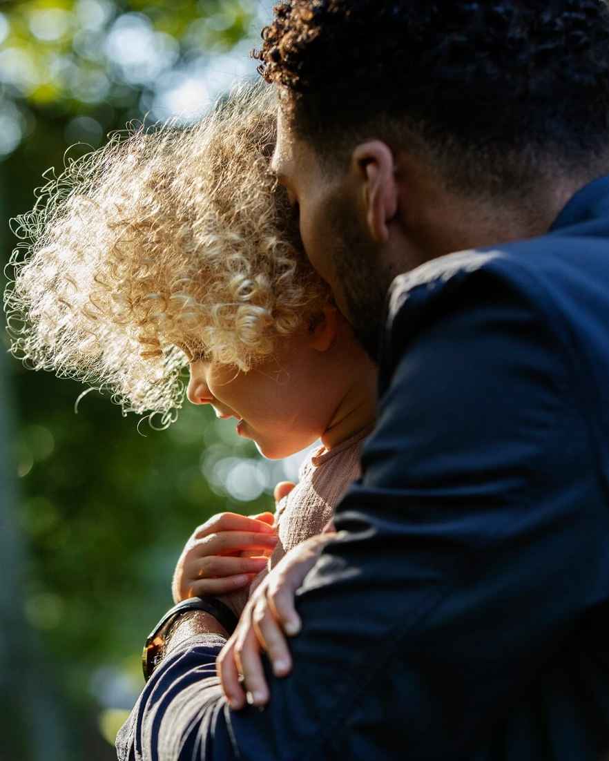 Een man houddt een kind dicht tegen zich aan. Het kind kijkt naar naar beneden.