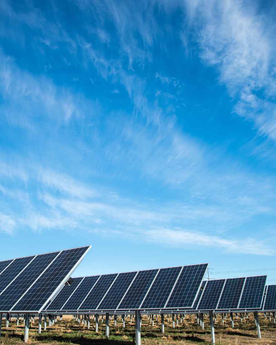 Rijen zonnepanelen staan in een open veld onder een blauwe lucht met witte wolken.