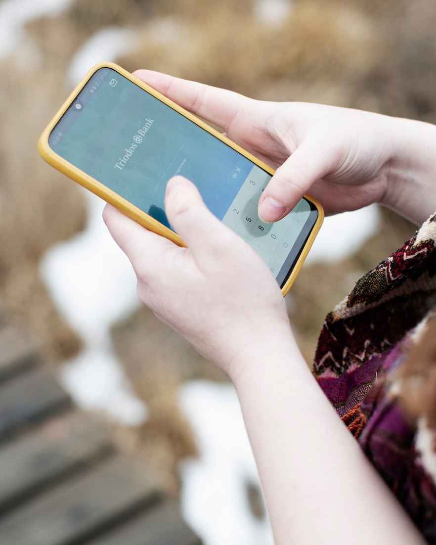 Een persoon houdt een smartphone vast en het startschem van de Triodos app is zichtbaar.