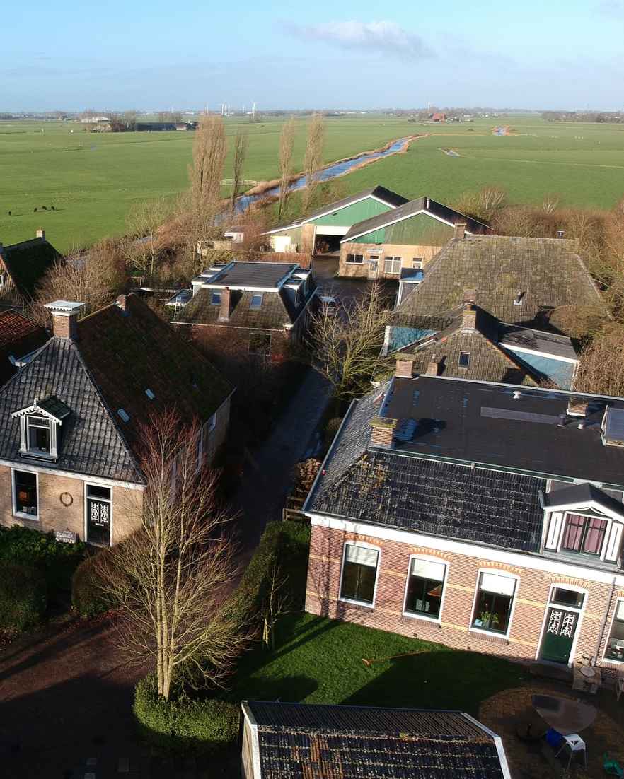 Luchtfoto van een dorp met huizen, bomen en groene weilanden op de achtergrond.