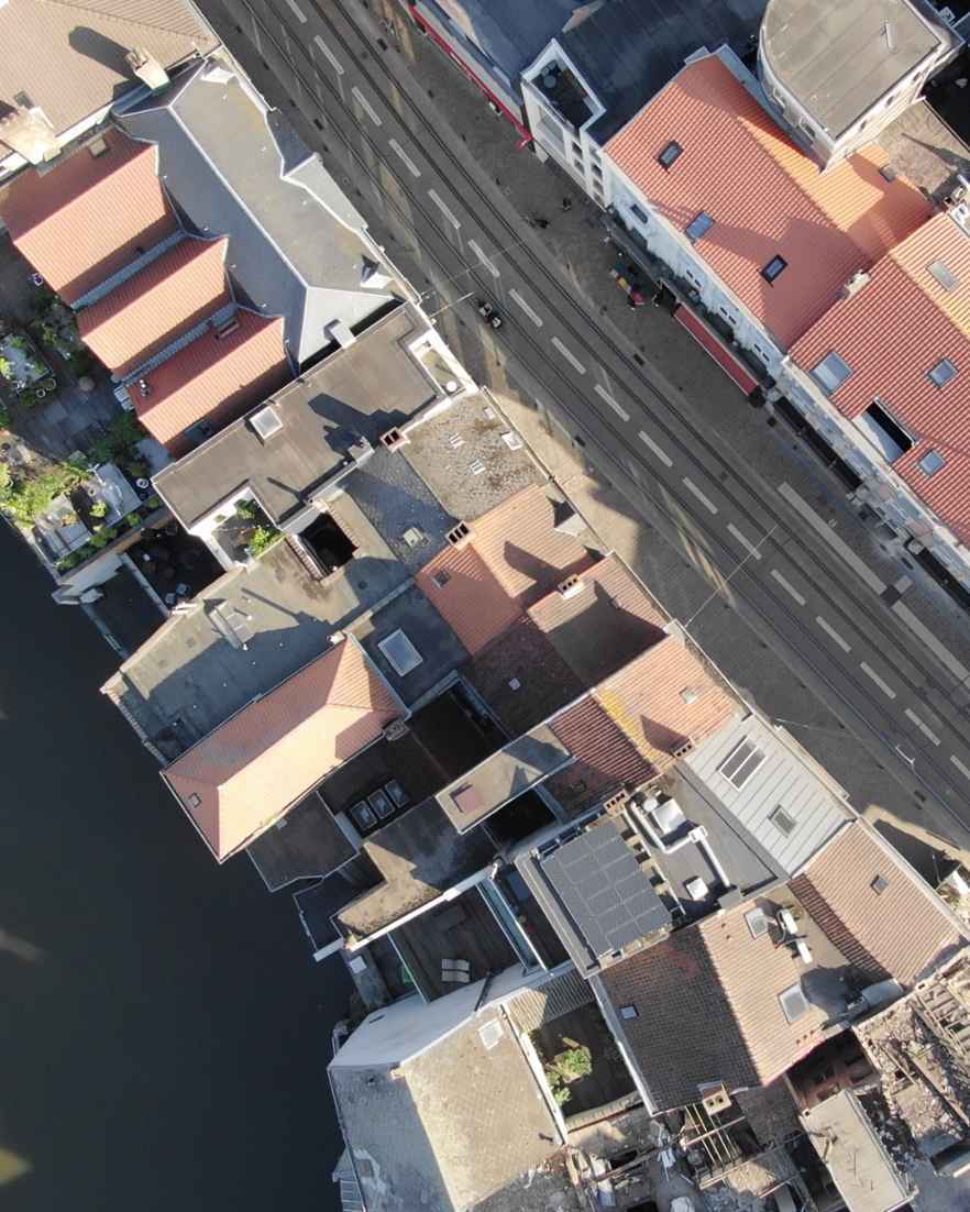 Luchtfoto van een straat langs het water met dicht op elkaar gebouwde huizen. Op de daken liggen zonnepanelen en lopen tramsporen door de straat.