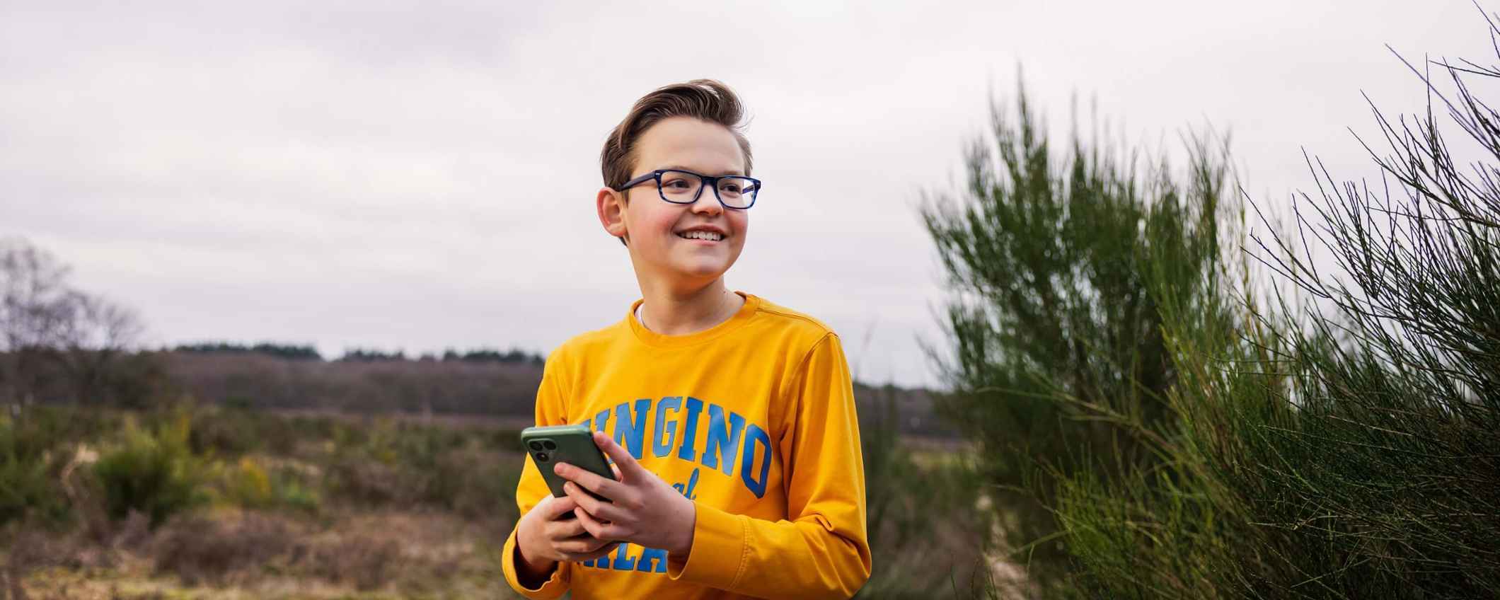 Een jongen staat buiten in de natuur en houdt een telefoon vast.