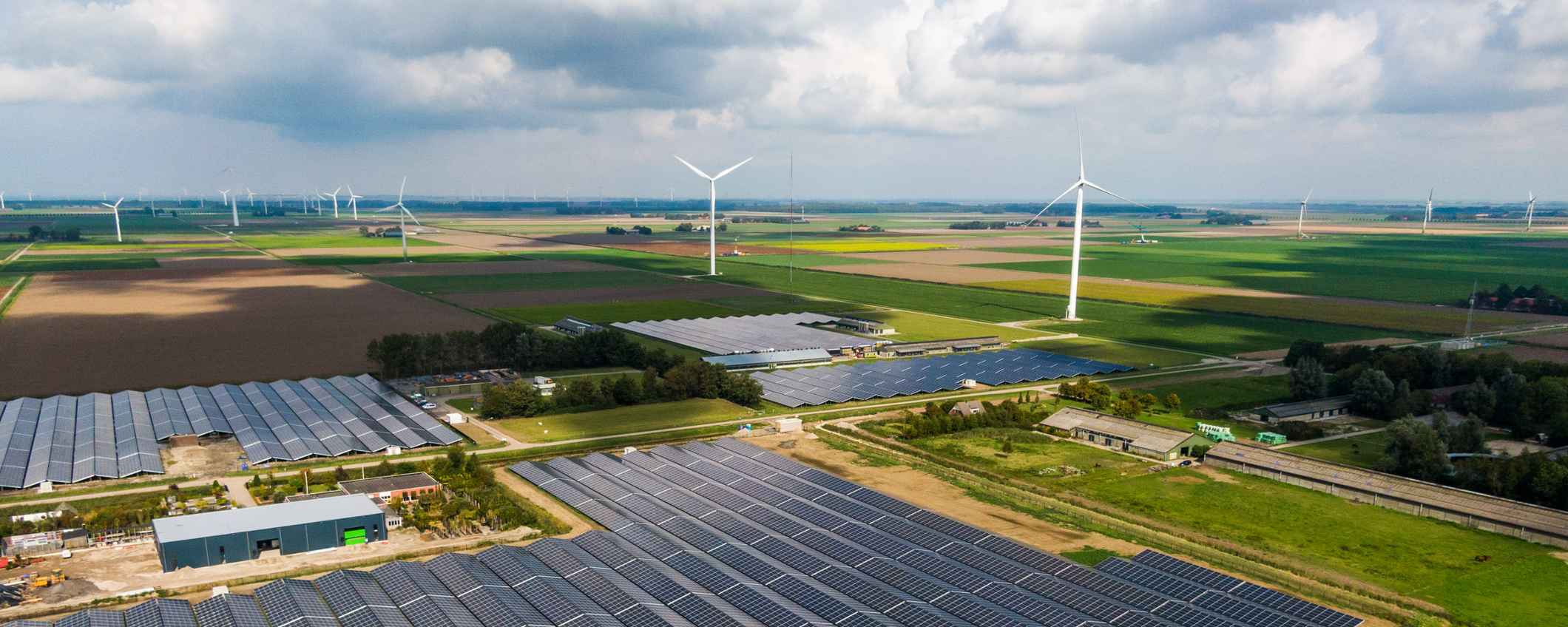 Luchtfoto van een landschap met zonnepanelen, windmolens, akkers en boerderijen.