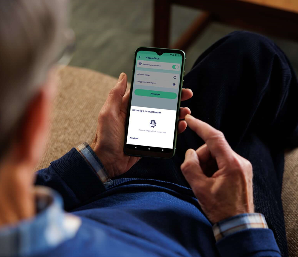 Een man zit op de bank en bevestigt een betaling op een smartphone met een vingerafdruk.