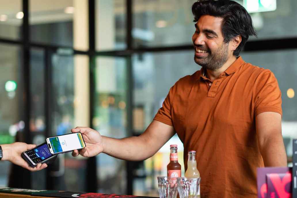 Een klant van Triodos Bank betaalt in een restaurant met Apple Pay op zijn telefoon