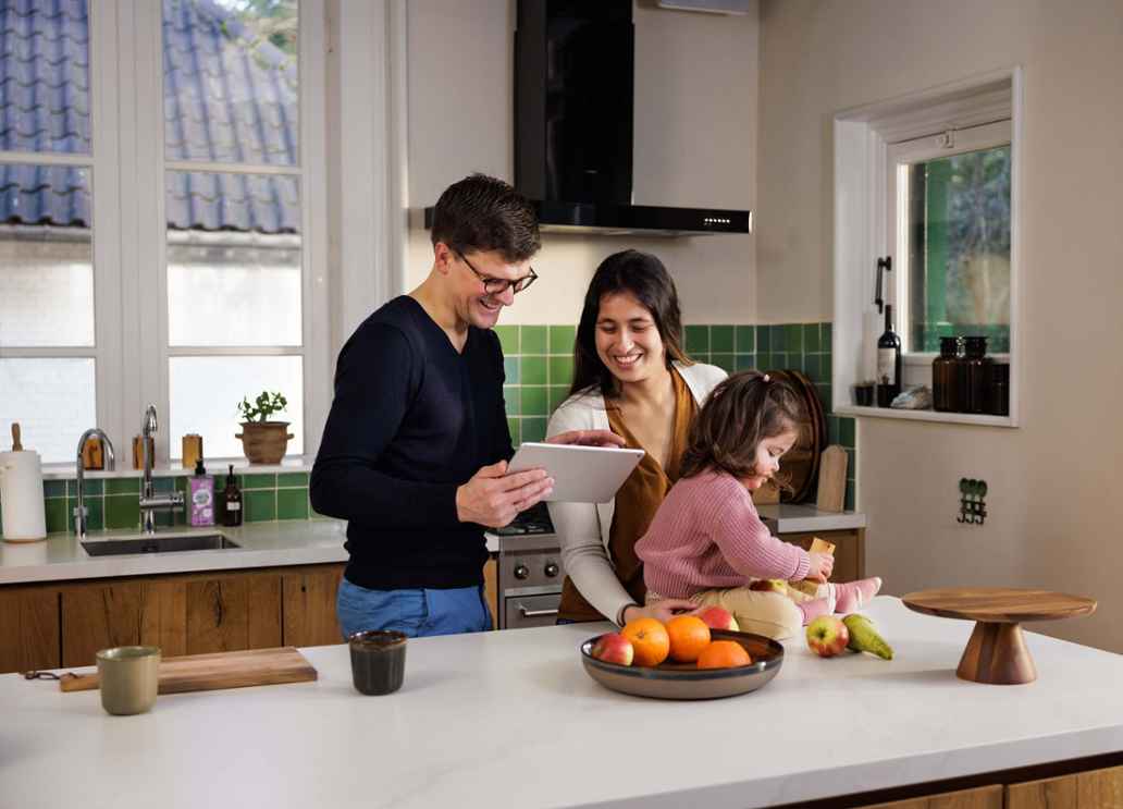 Man en vrouw staan met hun kind in de keuken. Het kind zit op het aanrecht en de man houdt een tablet vast.