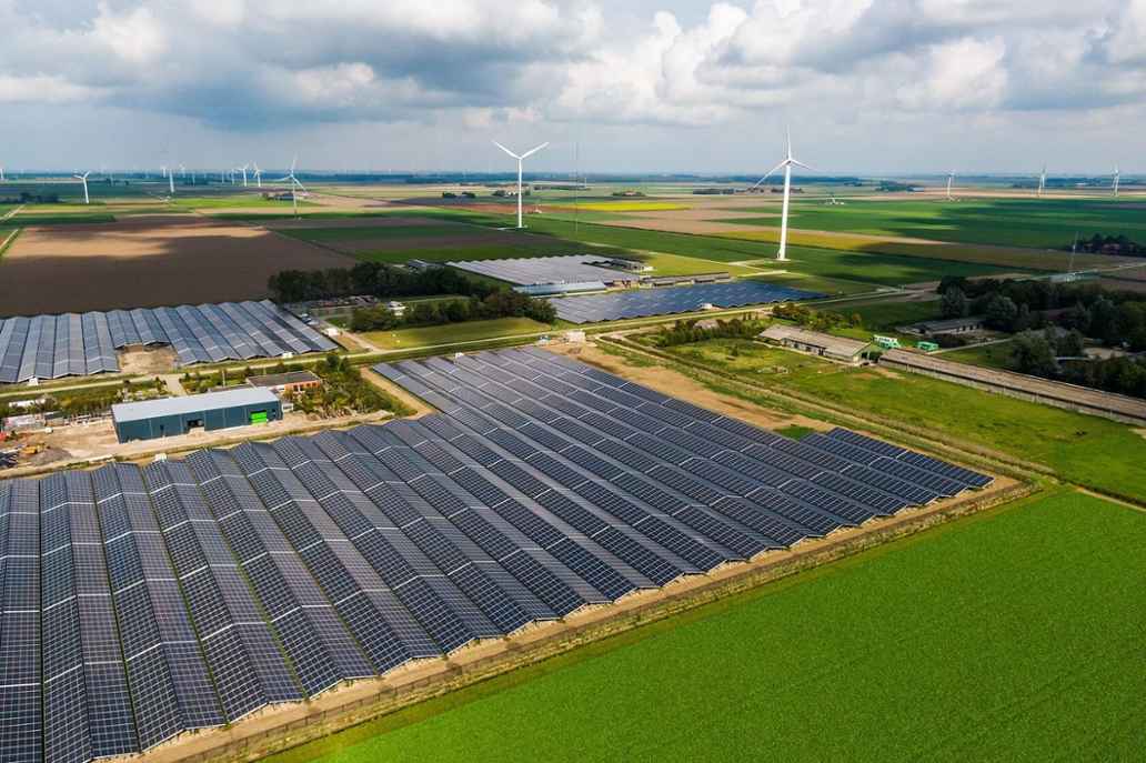 Luchtfoto van een landschap met zonnepanelen, windmolens, akkers en boerderijen.