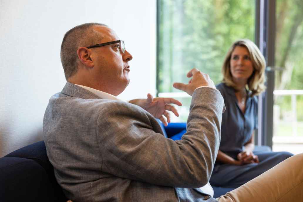 Léonhard ten Siethoff, directeur Triodos Foundation. Leonhard praat en zijn handen doen mee. Hij draagt een bril, gemillimeterd grijs haar en een grijs colbert. Verderop zit Riëlla Hollander, zij luistert naar hem.