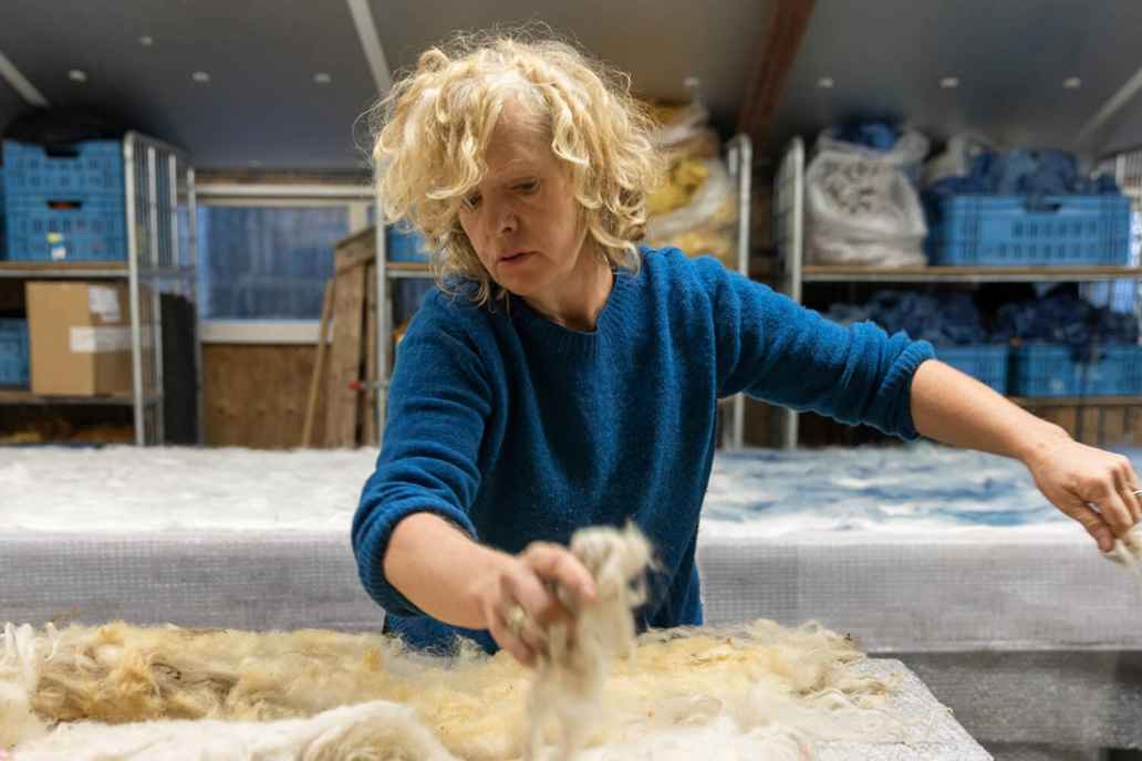 Een vrouw spreidt wol uit op een grote tafel in een werkruimte. Zij is de eigenaar van studie Claudy Jongstra en klant bij Triodos Bank.