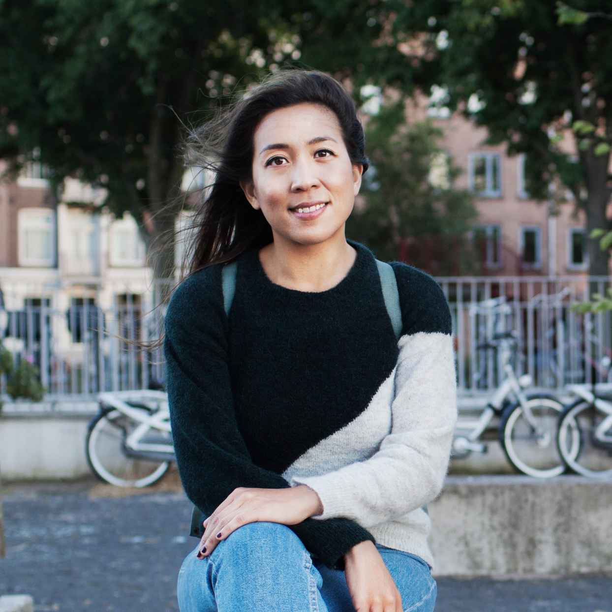 Vrouw met een rugtas zit op een bankje in een openbare ruimte.