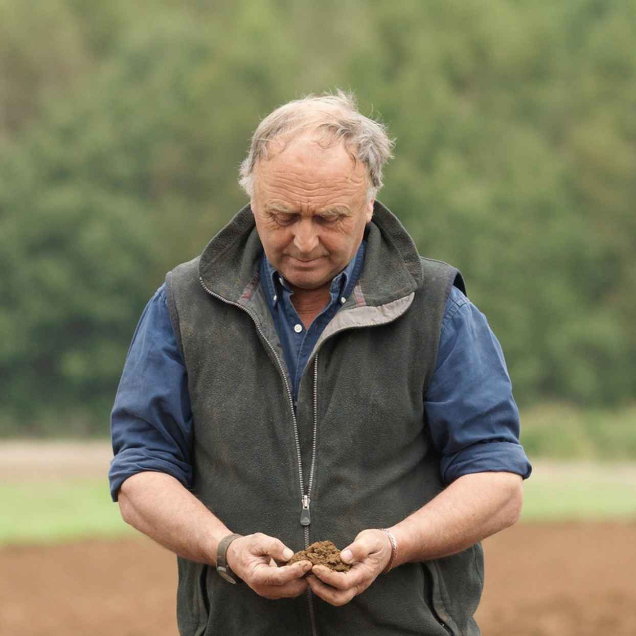 Een boer staat op een akker en houdt aarde in zijn handen.