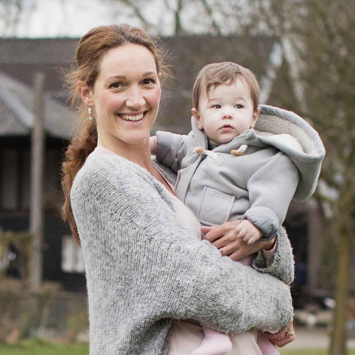 Vrouw houdt een klein kind vast en glimlacht en staat in een bosrijke omgeving.
