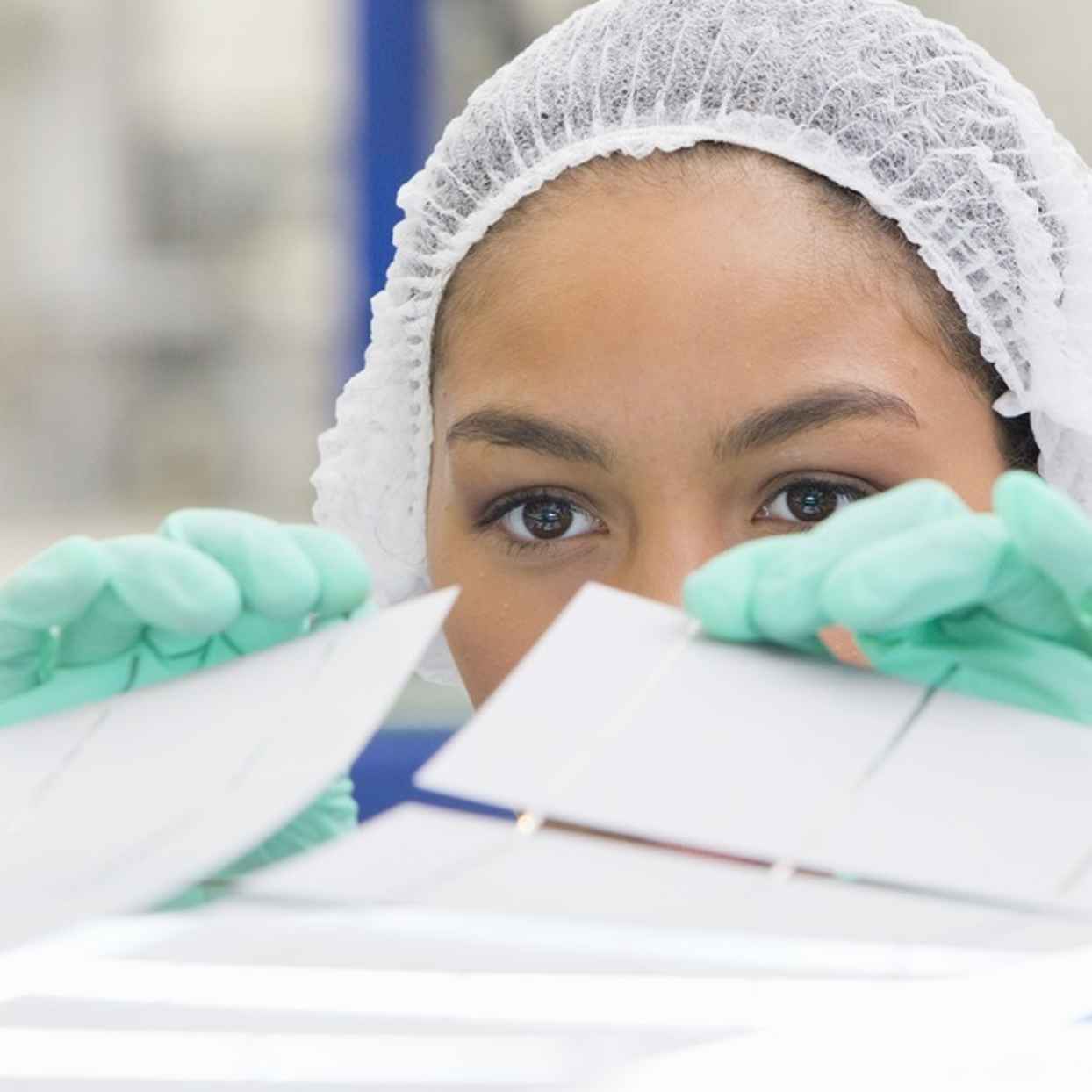 Een persoon draagt handschoenen en een haarnetje en bekijkt witte materialen aandachtig in een schone werkruimte.