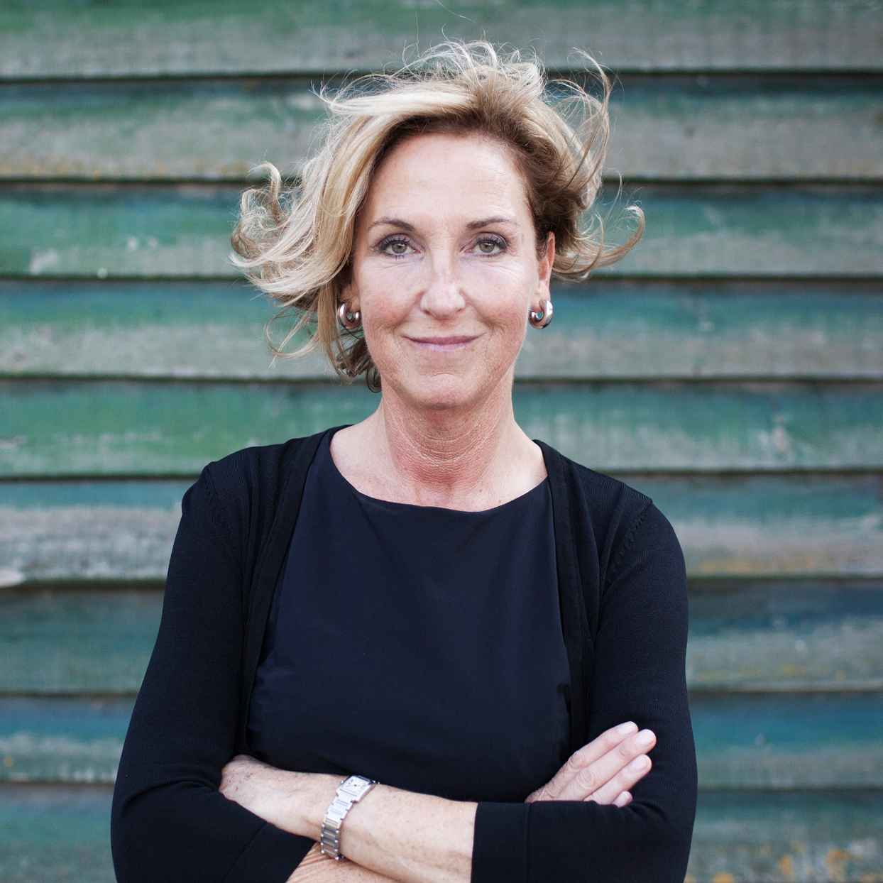 Vrouw met gekruiste armen staat voor een gebouw met groene planken.