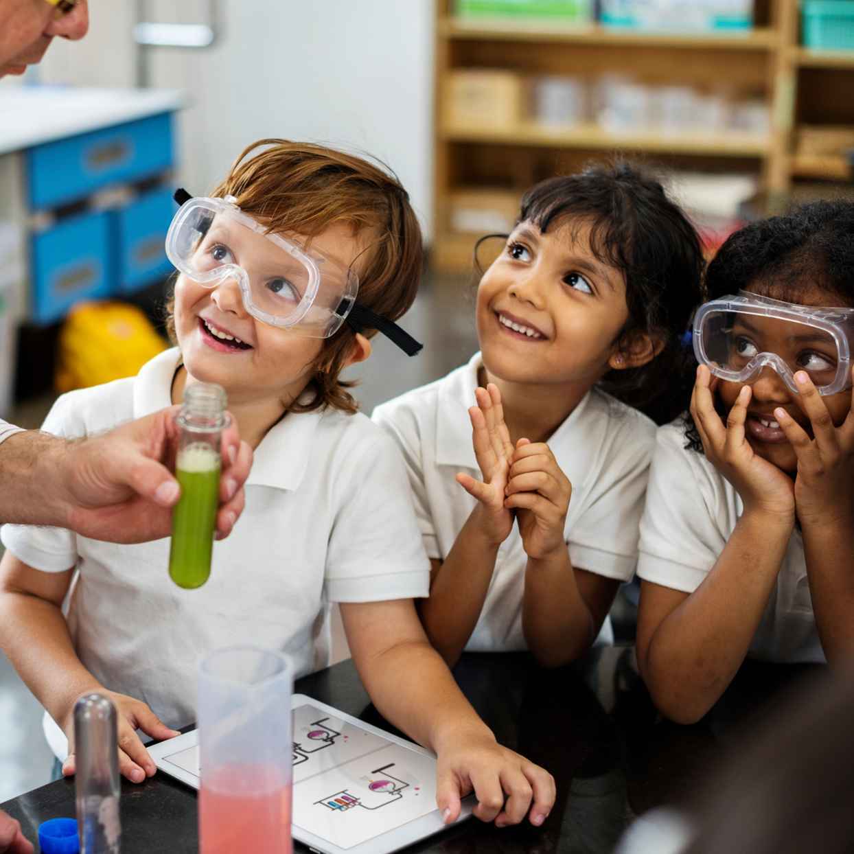 Een leraar laat een proefje zien aan kinderen in een klas. De kinderen kijken aandachtig mee.